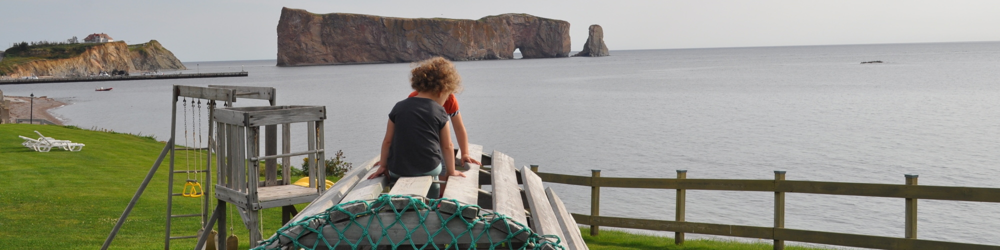 Enfants dans un module de jeux extérieurx, vue sur la mer et sur le rocher Percé