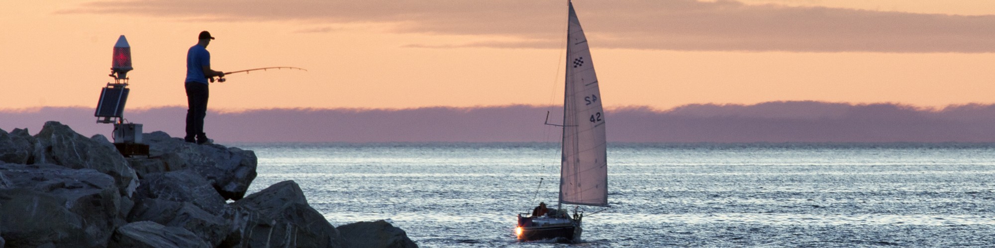 Pêcheur sur le bord de la mer, voilier à l'horizon