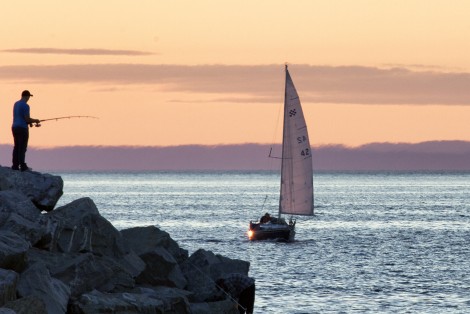 Pêcheur sur le bord de la mer, voilier à l'horizon