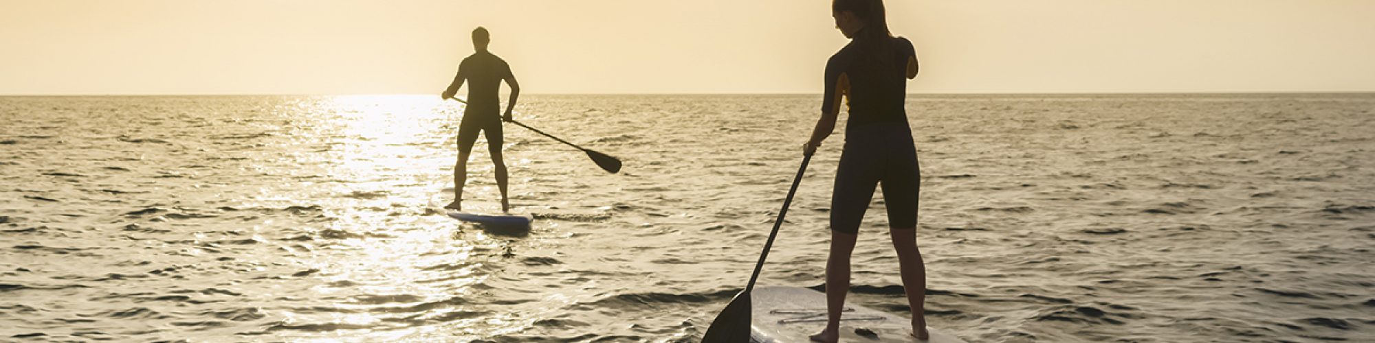 Man and woman doing standup paddling in sea during sunset.